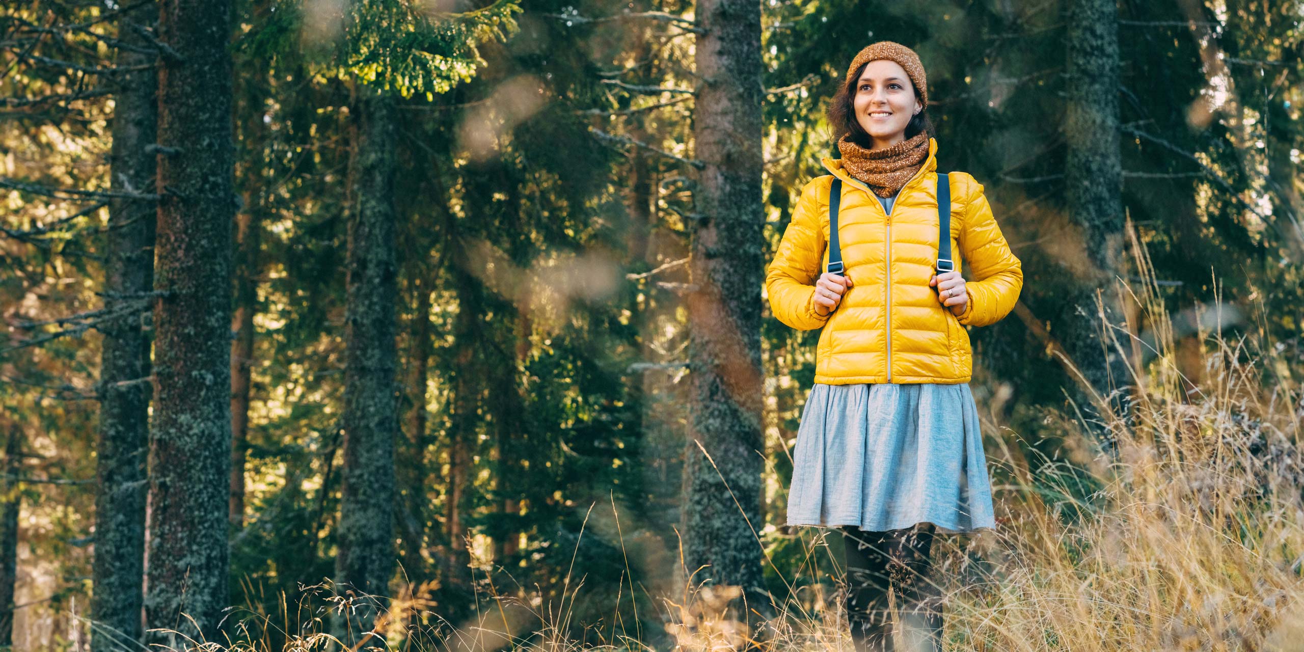 Junge Frau mit Rucksack bepackt steht an Waldstück